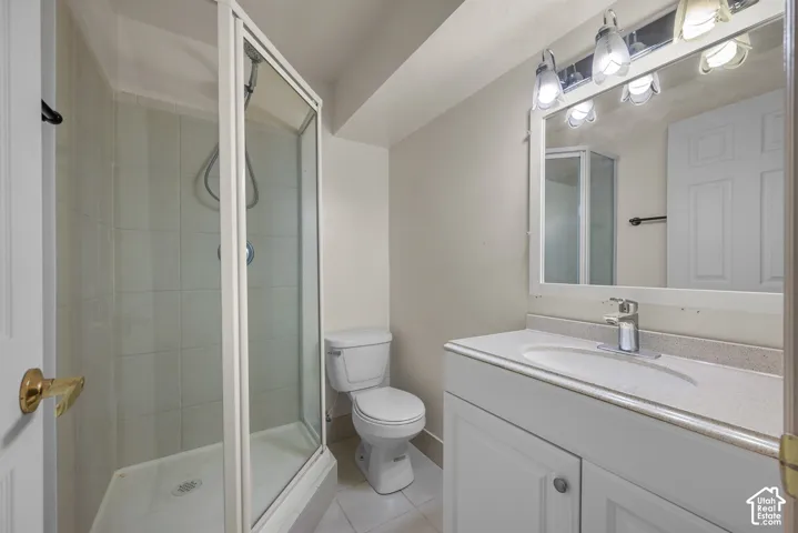 Bathroom featuring a glass-enclosed shower, white vanity with integrated sink, stone-finish countertop, and wall-mounted mirror with overhead lighting