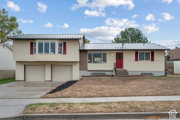 Split-level residence featuring a metal roof, light-colored siding, and a two-car garage