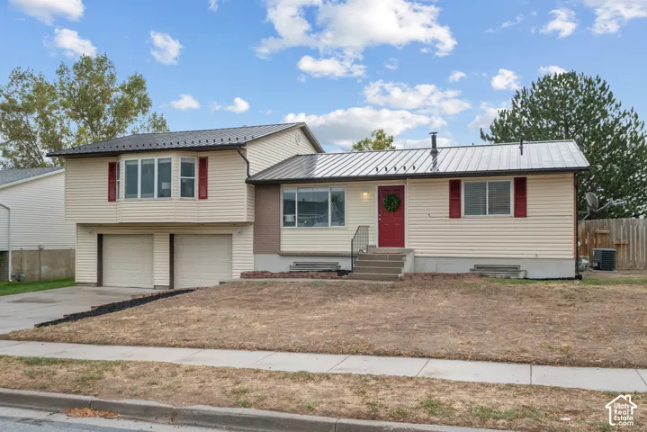 Split-level residence featuring a metal roof, light-colored siding, and red accent shutters