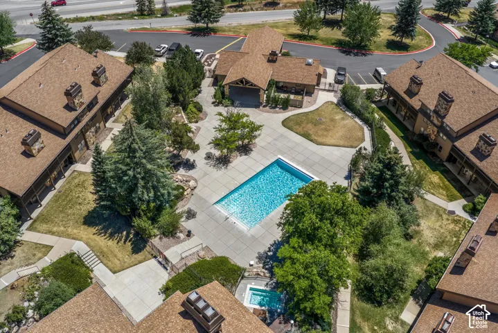 Outdoor swimming pool, separate hot tub, paved patio areas, surrounding mature landscaping, and multi-story buildings with brown shingle roofs