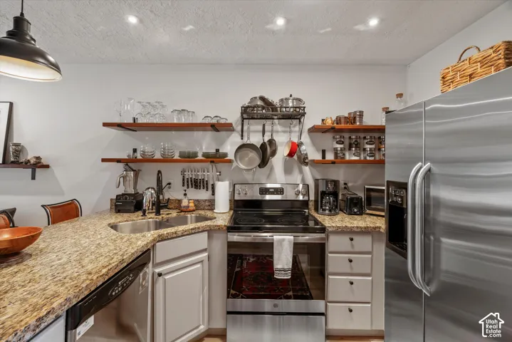 Granite-style countertop with an undermount sink, stainless steel appliances, white cabinetry, and open wood-finish shelving