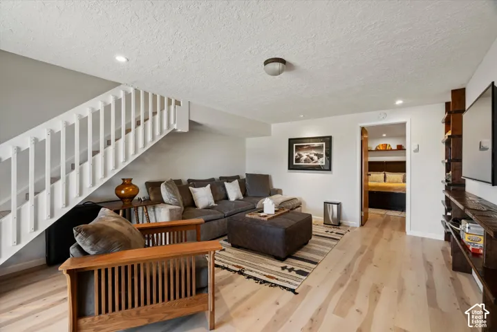 Light wood-finish flooring, white painted staircase, recessed ceiling lighting, and built-in wood shelving