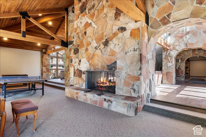 Stone-clad fireplace with a hearth, wood-finish vaulted ceiling with exposed beams, recessed lighting, and stone arched doorways