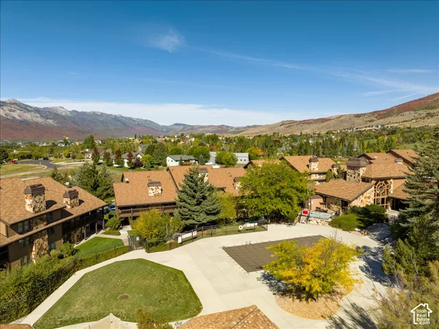 Community with mountain scenery, multiple buildings featuring stone and shingle exteriors, central courtyard with green space, and an outdoor pool area