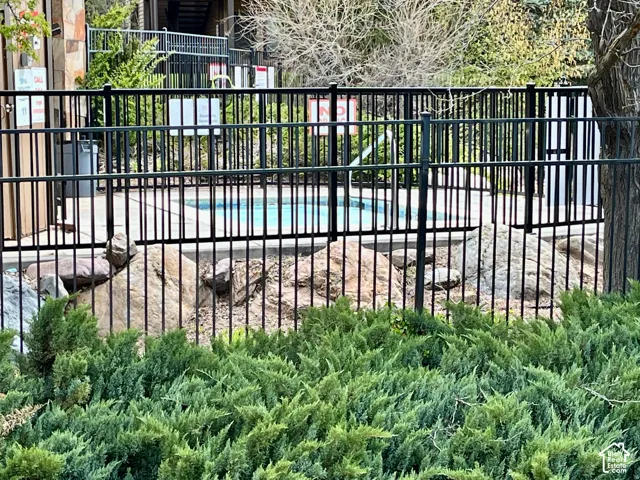 Fenced pool area featuring a blue-tiled pool, surrounding rock landscaping, and a black metal fence