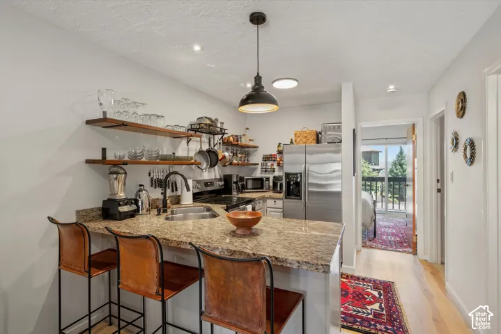 Kitchen featuring stone-look countertops, stainless steel appliances, open wood shelving, and a peninsula with seating