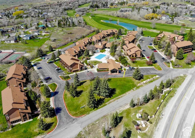 Community featuring multiple buildings with brown shingle roofs, surrounded by mature trees, paved parking areas, and green landscaping