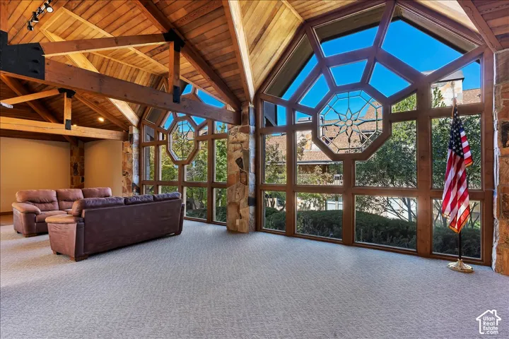 Vaulted wood-paneled ceiling with exposed beams, full-height multi-pane windows, stone columns, and light-colored carpeting