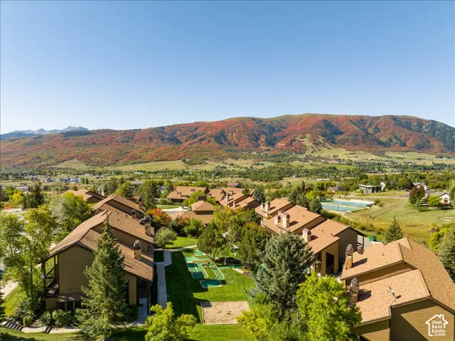 Community grounds featuring mature trees, green spaces, and recreational courts, set against a mountainous backdrop