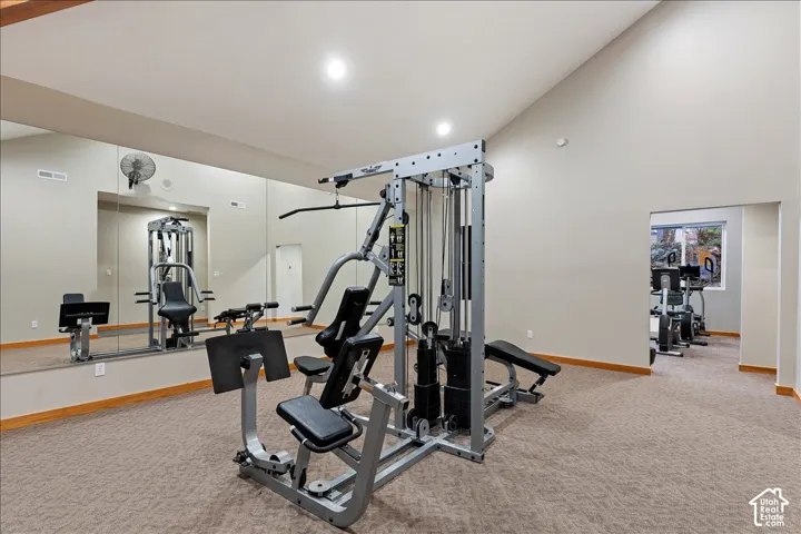 Dedicated fitness area featuring extensive mirrored walls, a vaulted ceiling, recessed lighting, and carpeted flooring