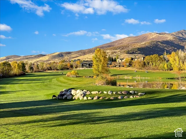 Expansive green golf course with a tranquil pond, surrounded by mature trees and distant mountains
