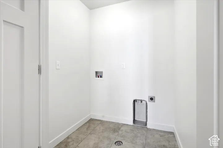 Dedicated laundry space featuring white walls, a white solid core door, and gray tile flooring