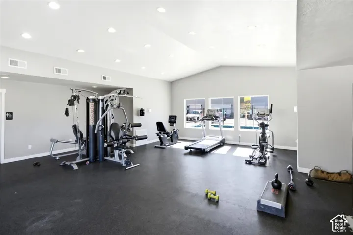 Spacious fitness area featuring a vaulted ceiling with recessed lighting, rubber flooring, and multiple windows