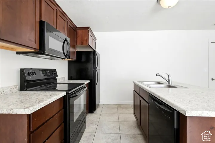 Kitchen featuring dark wood-finish cabinetry, light-colored countertops, black appliances, a double basin sink with a chrome faucet, and tiled flooring
