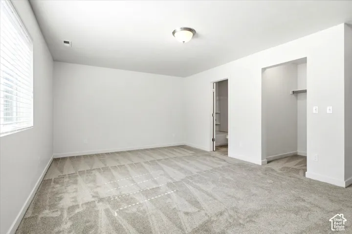 Bright room featuring light gray carpet, white walls, a ceiling-mounted light fixture, and an open doorway leading to an adjoining space