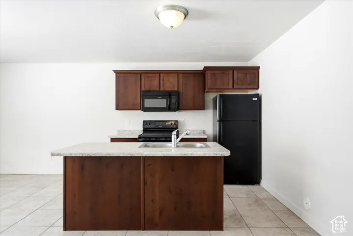 Kitchen featuring wood-finish cabinetry, light-toned countertop, stainless steel sink, and tile flooring