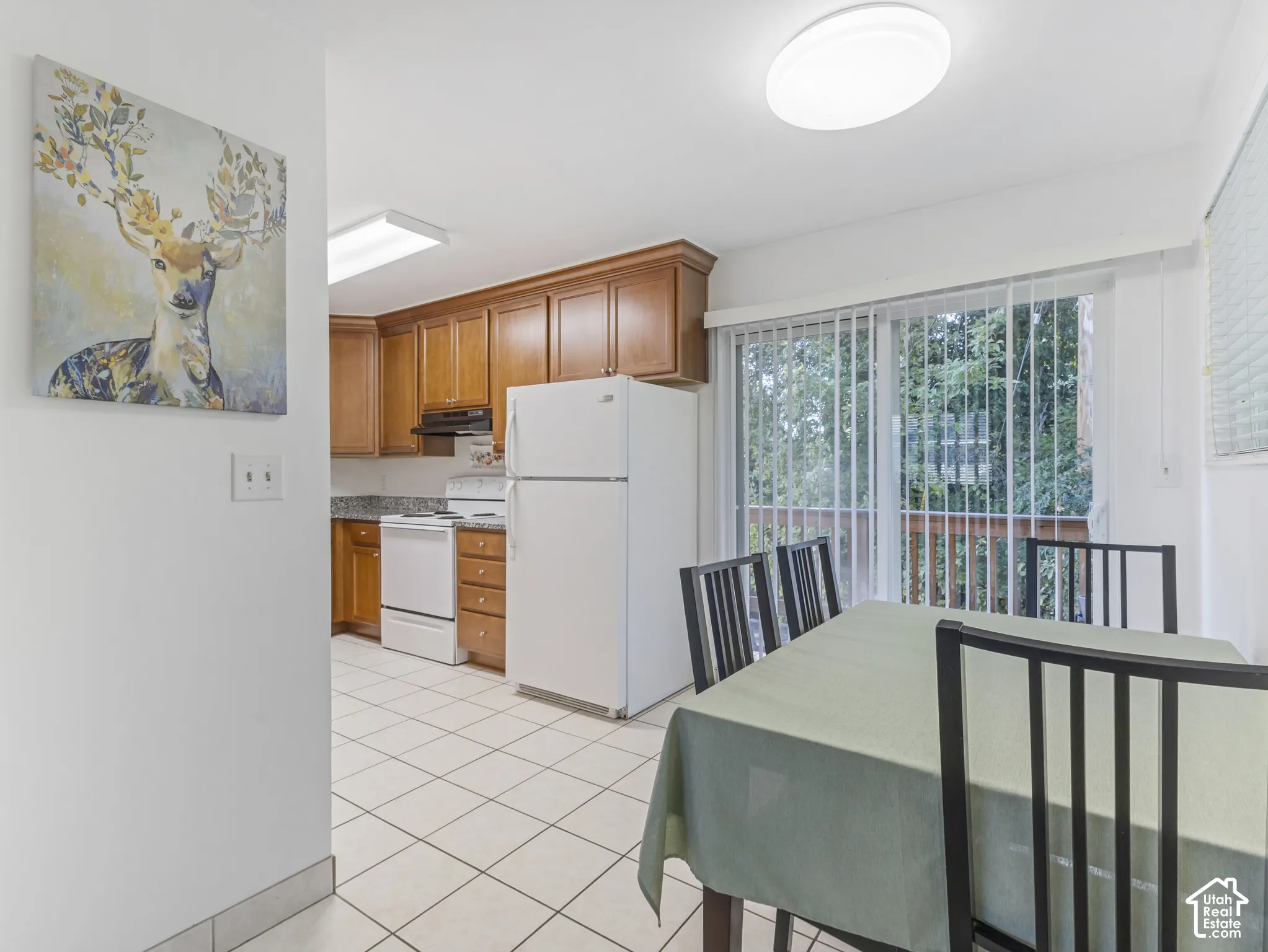 Kitchen featuring wood cabinetry, white appliances, and light-toned tile flooring