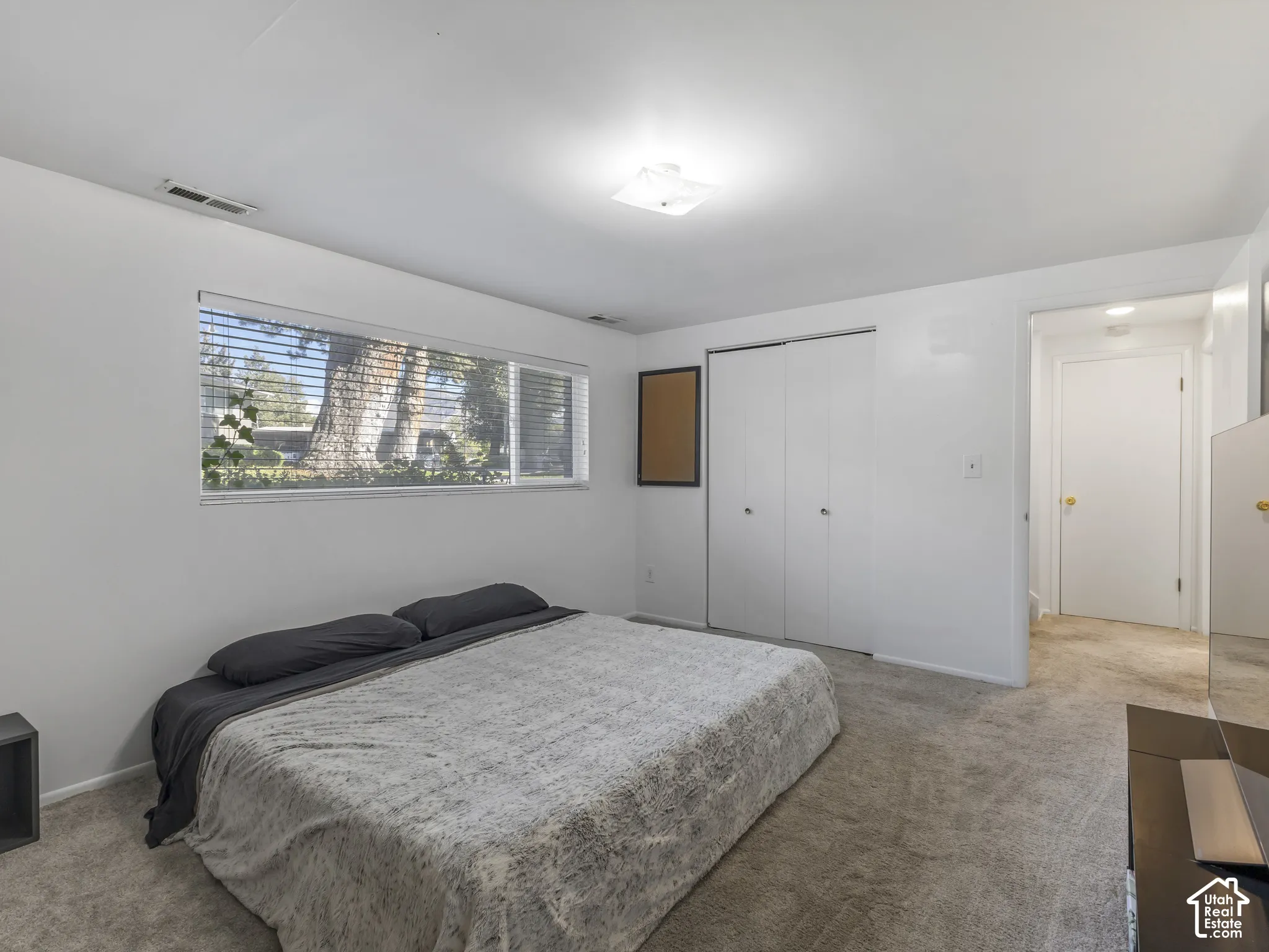 Carpeted flooring, white walls, horizontal window with blinds, bi-fold closet doors, and flush-mount ceiling light fixture