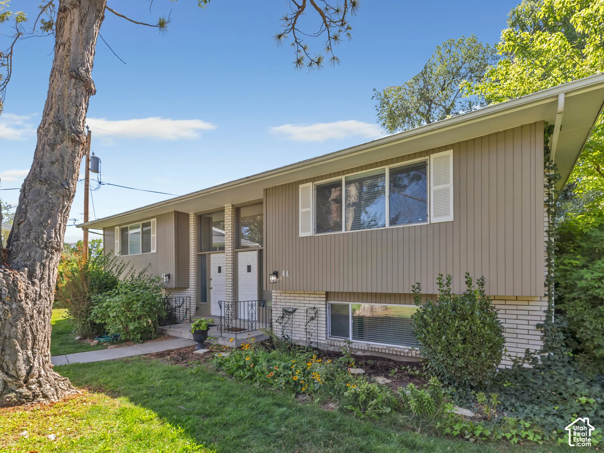 Split-level exterior featuring vertical siding, white window shutters, and a brick foundation