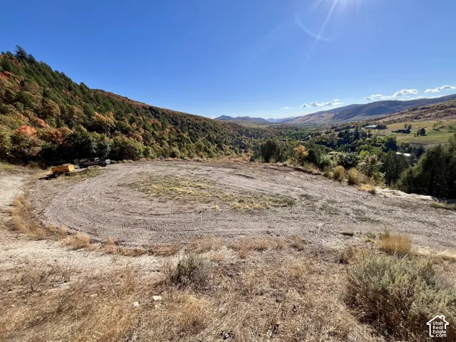 Expansive graded lot with surrounding hillsides, varied foliage, and distant mountain ranges