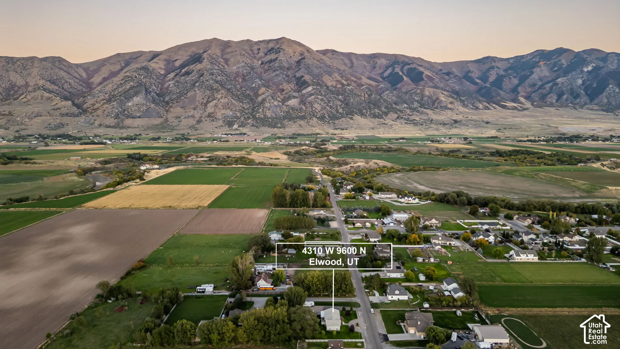 Expansive rural setting with agricultural fields, mature trees, and mountainous terrain