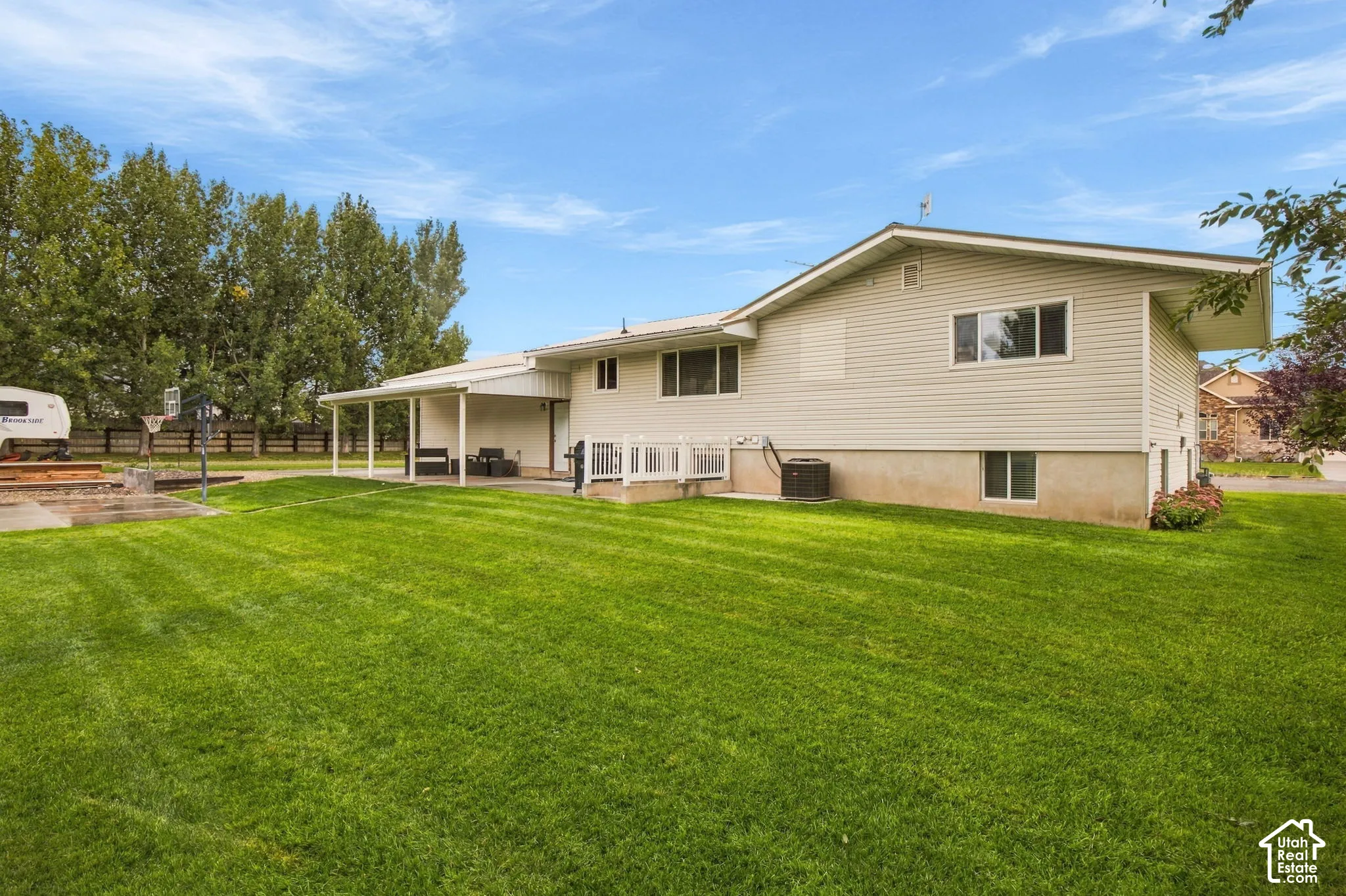Expansive lawn with a covered patio, white deck railing, and mature perimeter trees