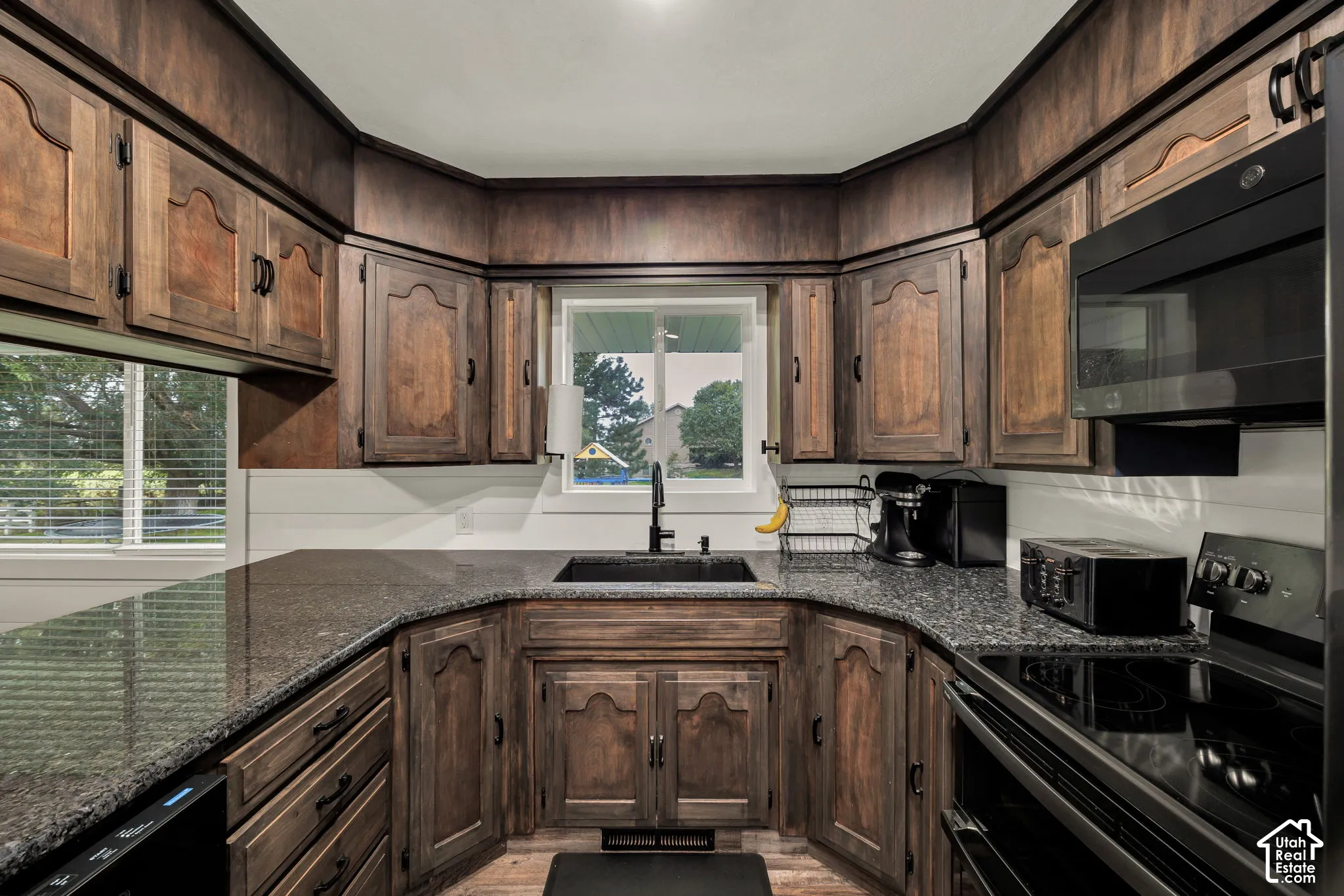 U-shaped kitchen featuring dark wood cabinetry, speckled countertops, a black sink with a matching faucet, and white horizontal paneling