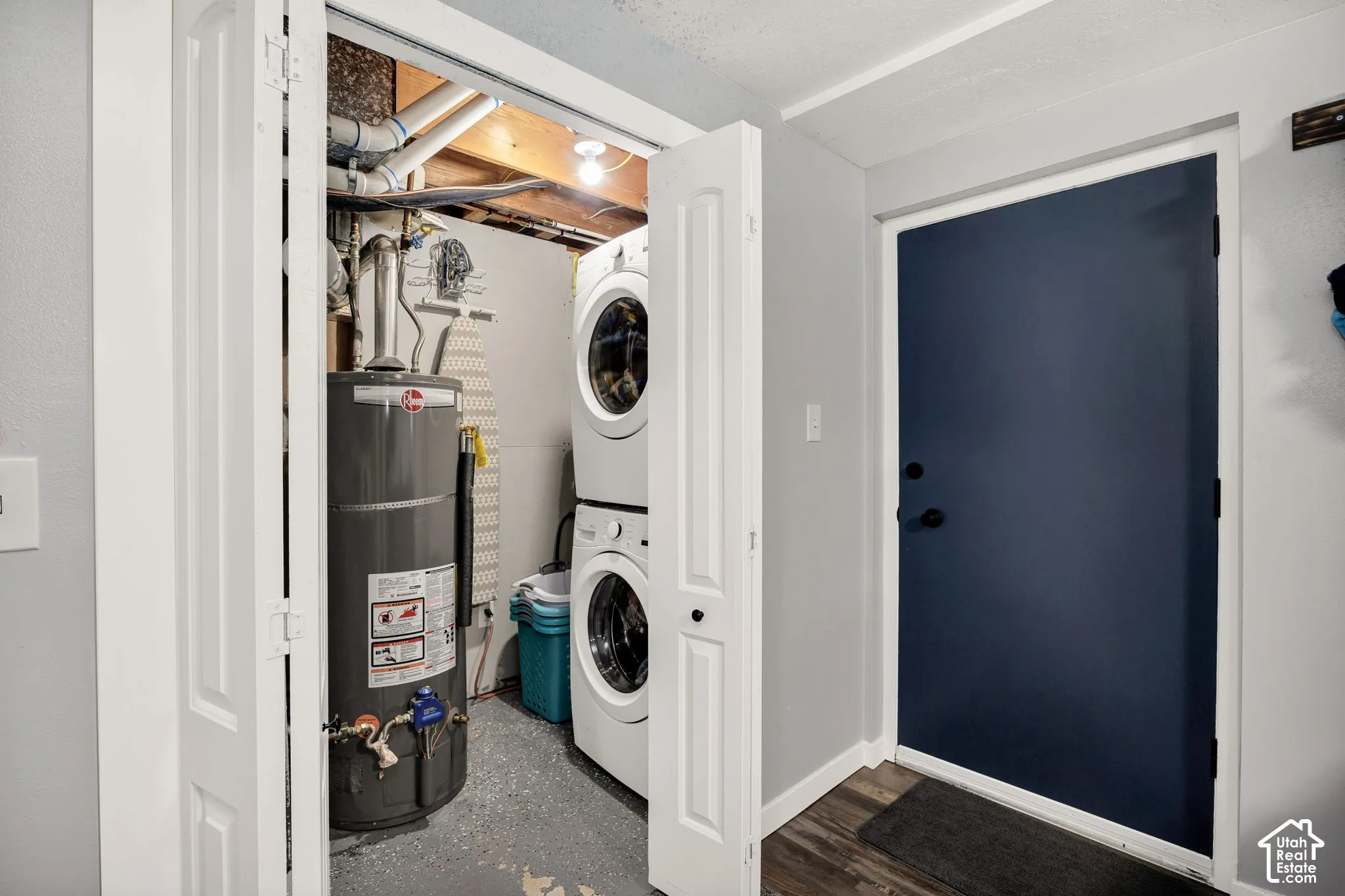 Utility closet featuring a water heater and stacked washer/dryer unit