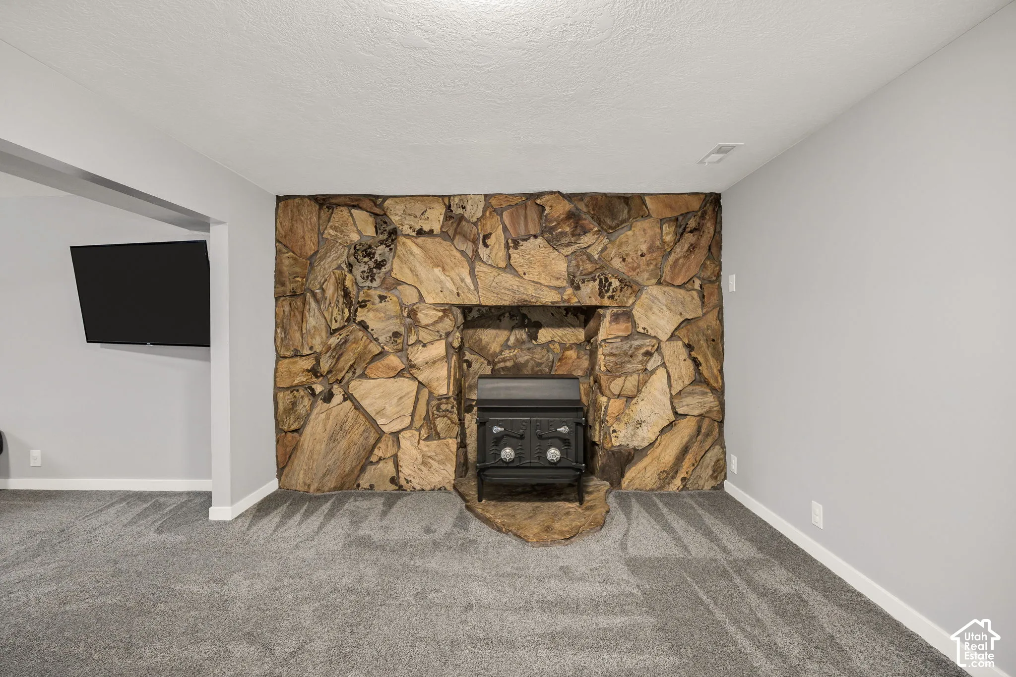 Stone-clad fireplace with a black wood-burning insert, framed by light gray walls and gray carpet