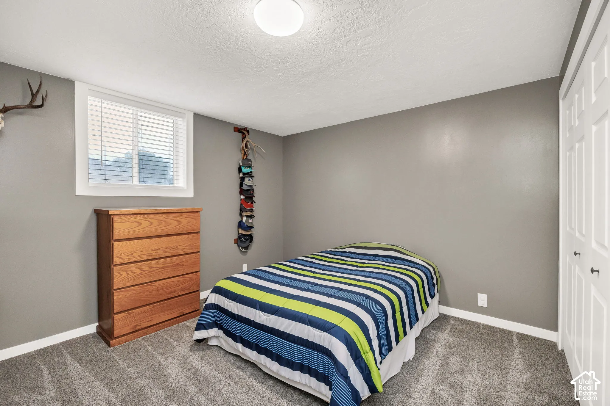 Recessed window with white blinds and trim, light gray walls, textured ceiling, gray carpet, and white bi-fold closet doors