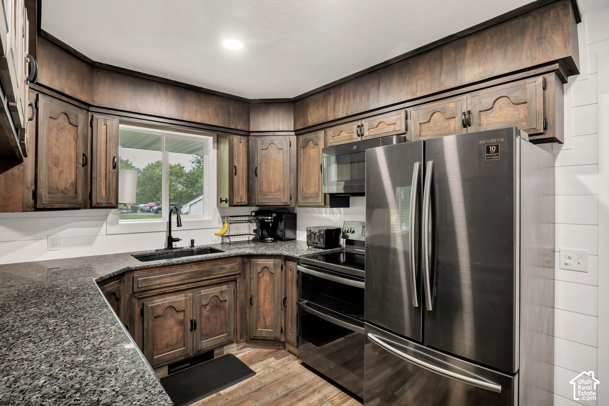 Kitchen featuring wood cabinetry, dark speckled countertops, stainless steel appliances, and a window above the sink