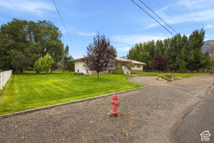 Expansive green lawn, white picket fencing, mature trees, gravel driveway, and a stone-clad foundation