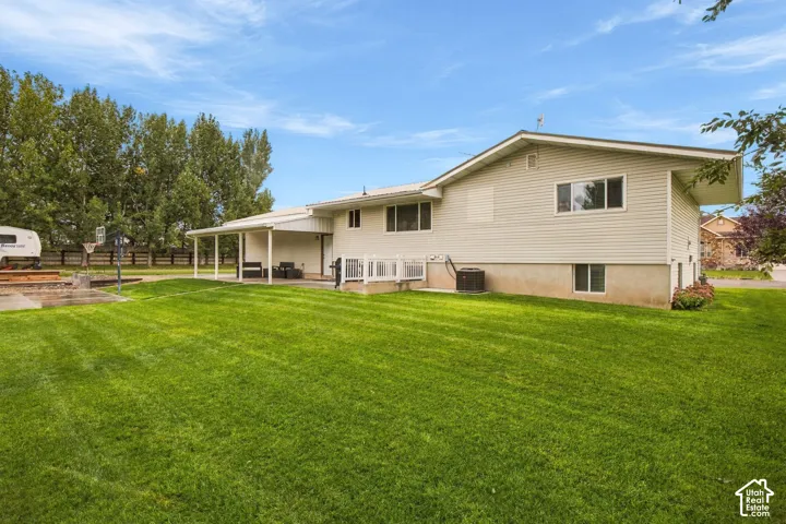 Expansive lawn with a covered patio, white deck railing, and mature perimeter trees