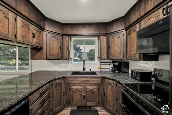U-shaped kitchen featuring dark wood cabinetry, speckled countertops, a black sink with a matching faucet, and white horizontal paneling