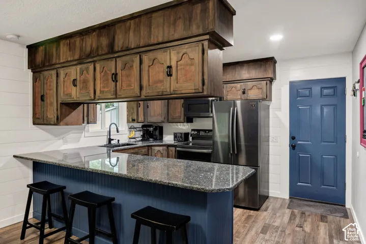 Kitchen featuring a peninsula with granite-finish countertop, wood-finish cabinetry, stainless steel appliances, and wood-finish flooring