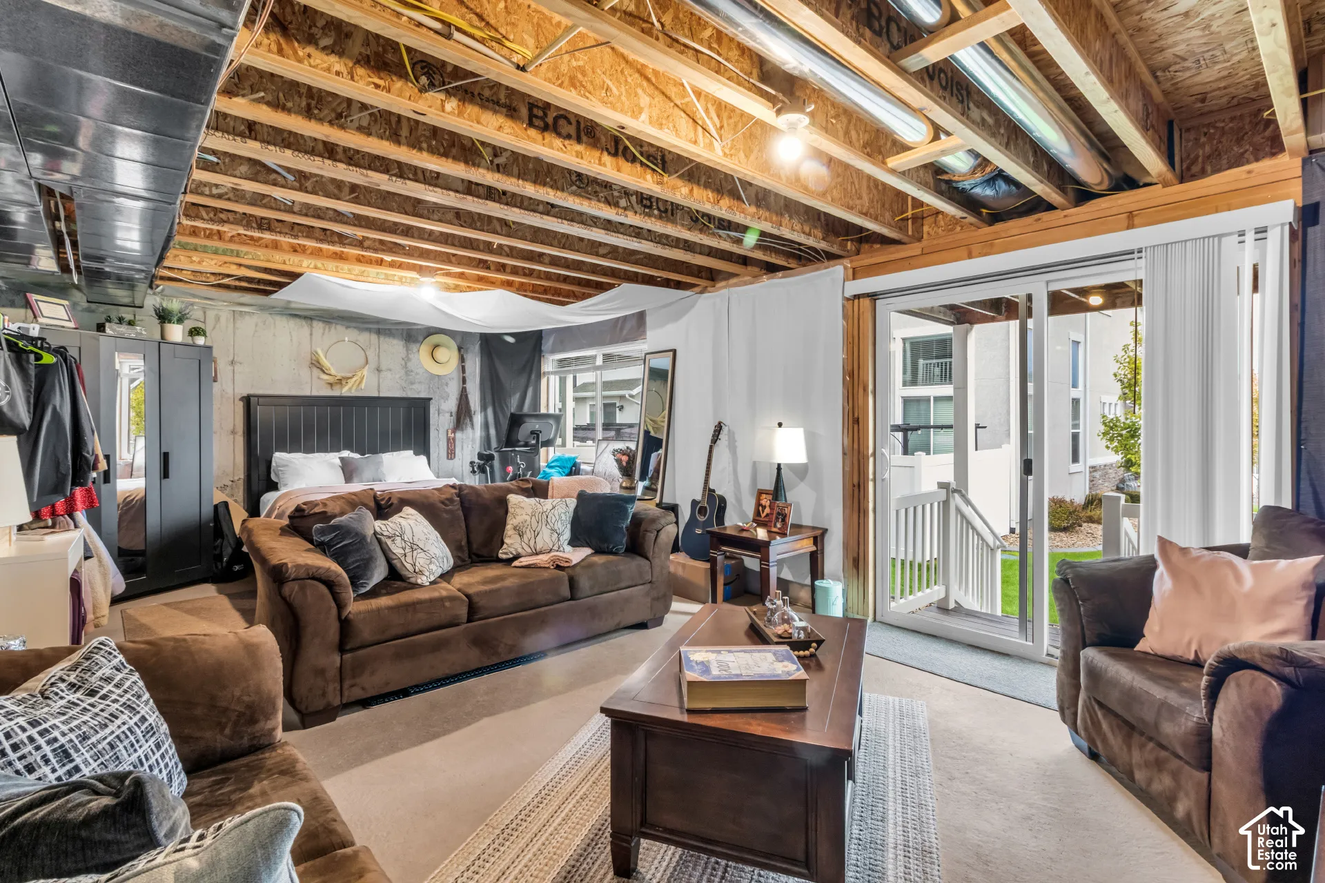 Sliding glass door leading to an exterior patio with stairs, exposed ceiling joists, concrete foundation walls, and carpet flooring