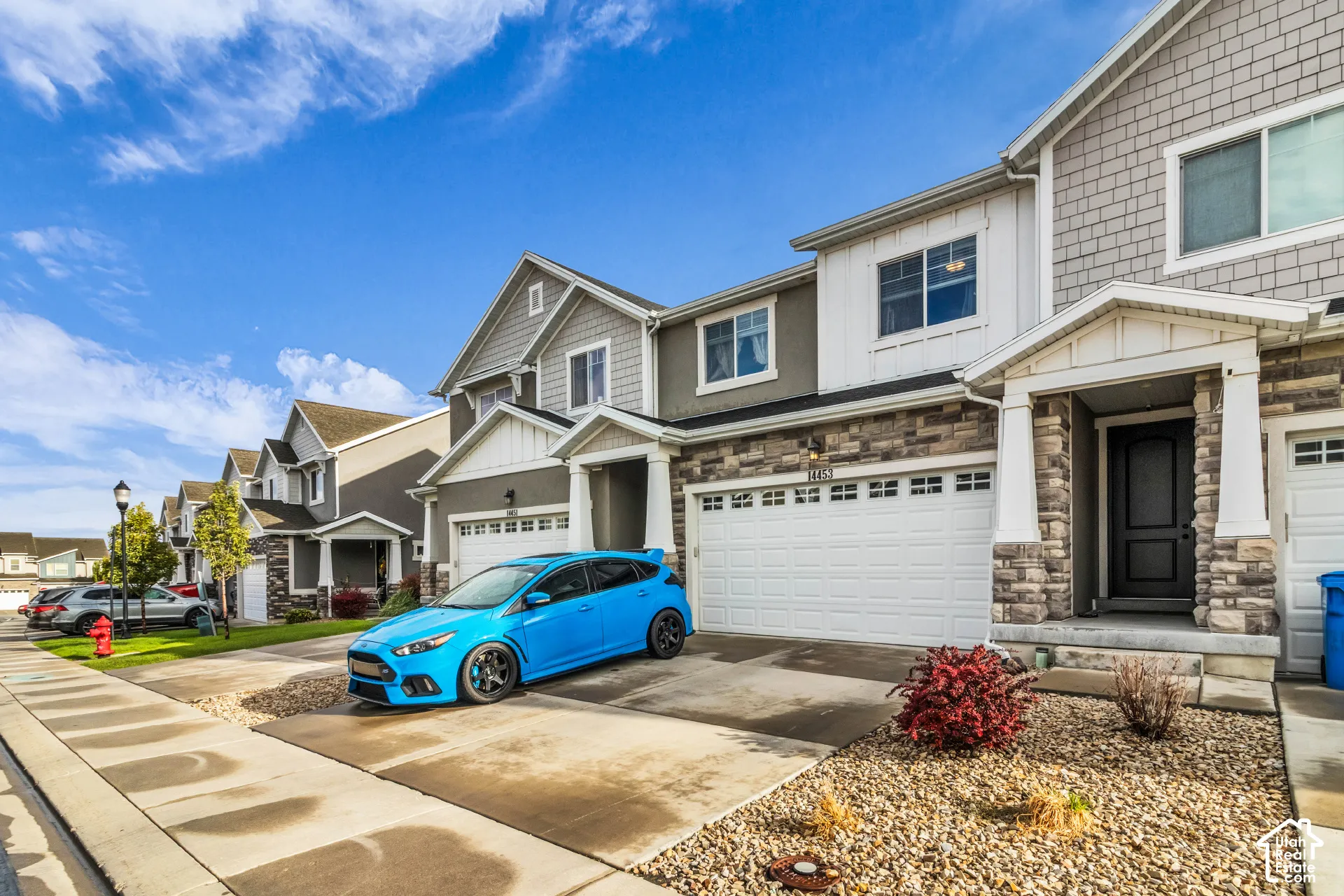 Two-story residence featuring a stone and siding exterior, an attached garage, a covered entry, a dark-toned front door, and a gravel and rock landscaping bed
