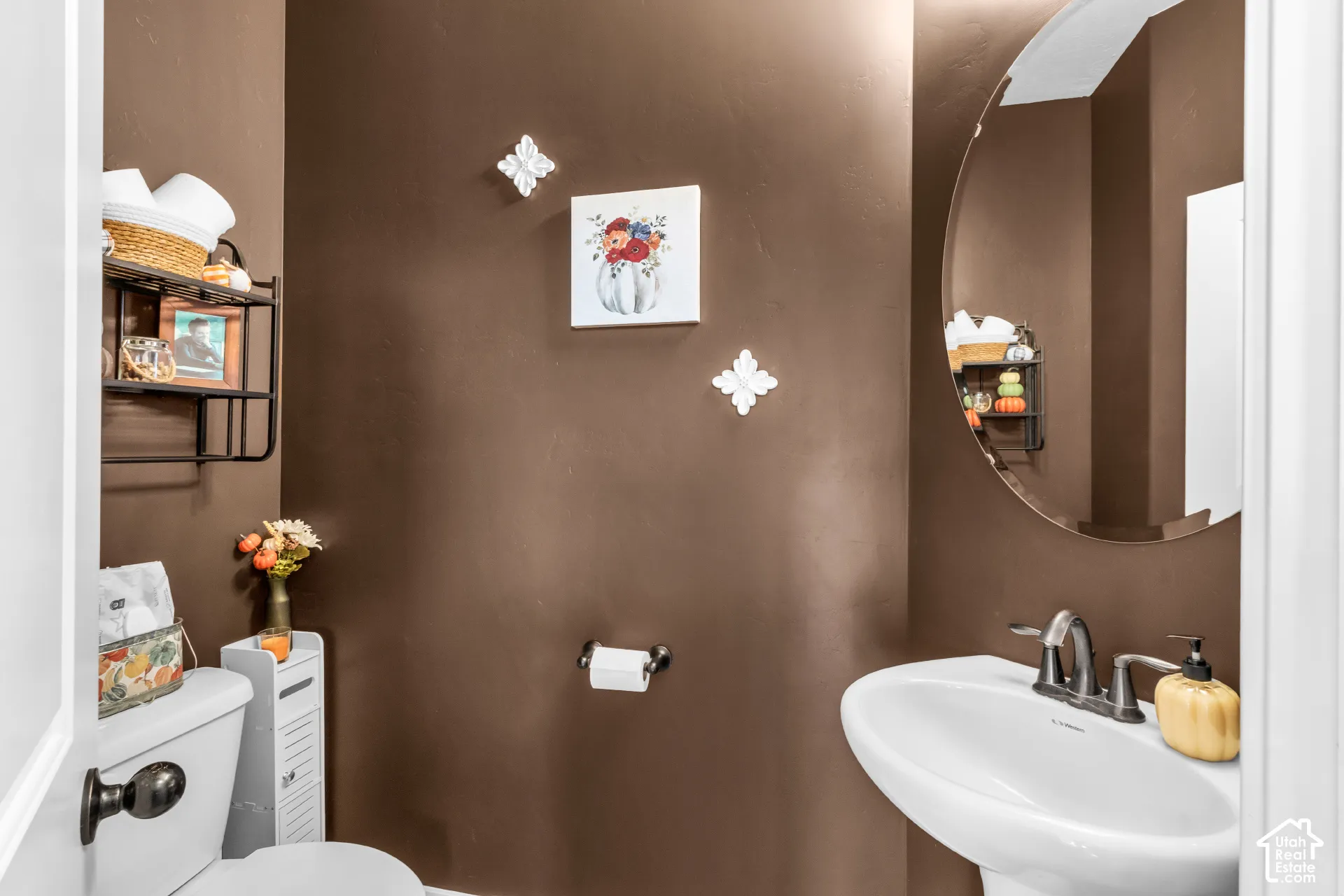 Pedestal sink with a brushed nickel faucet, rounded wall mirror, and a wall-mounted toilet paper holder