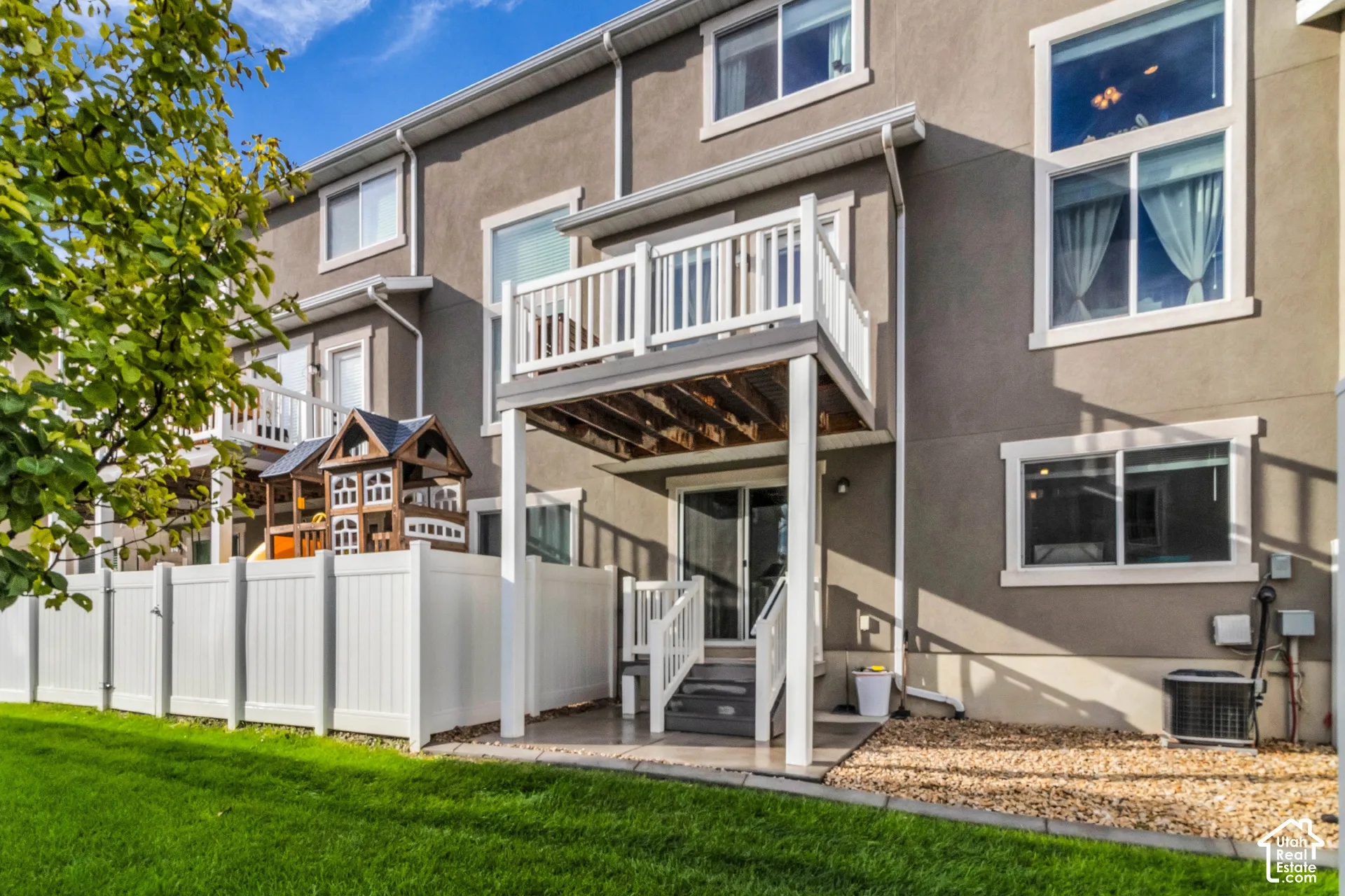 Exterior stucco finish, private balcony, ground-level patio, white vinyl fencing, and a manicured lawn