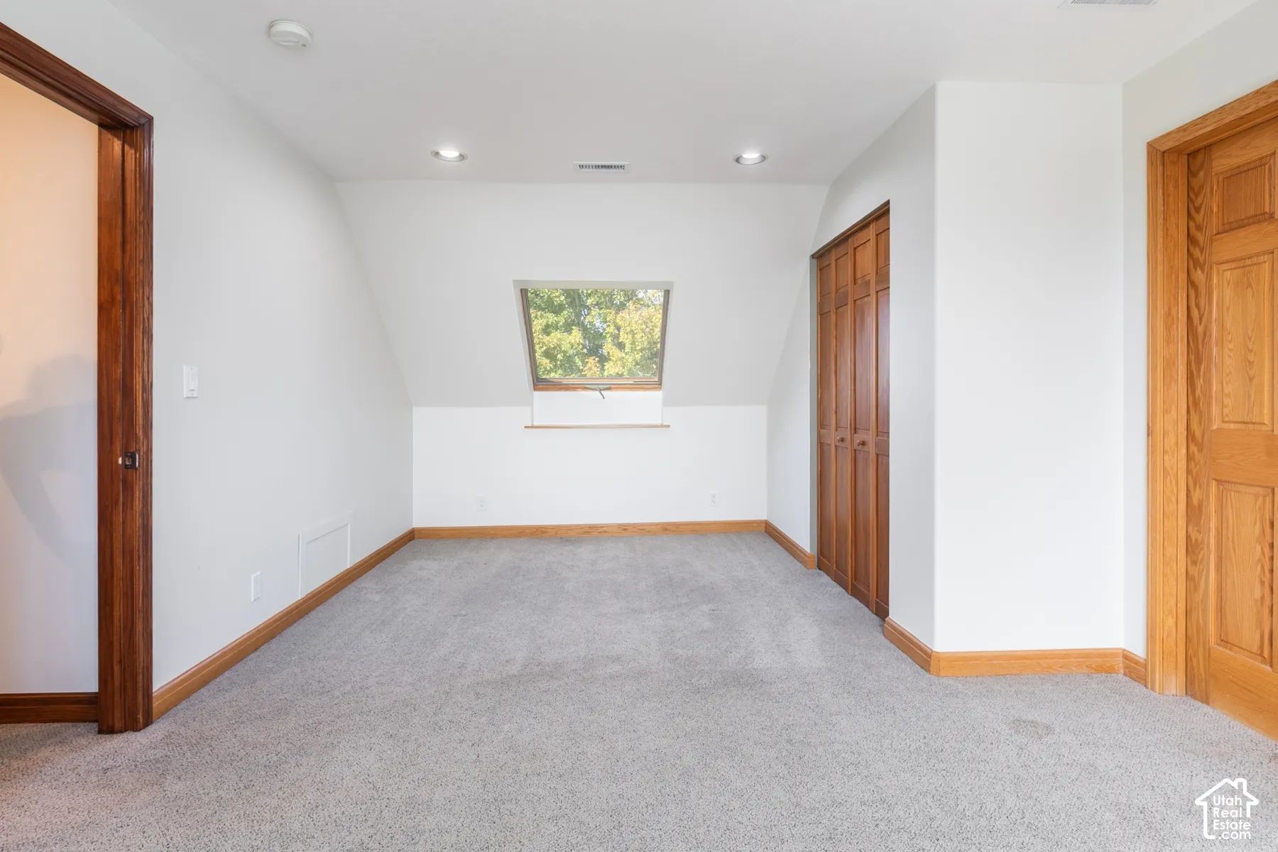 Room featuring light gray carpeting, white walls, natural wood-finish trim, and a window dormer
