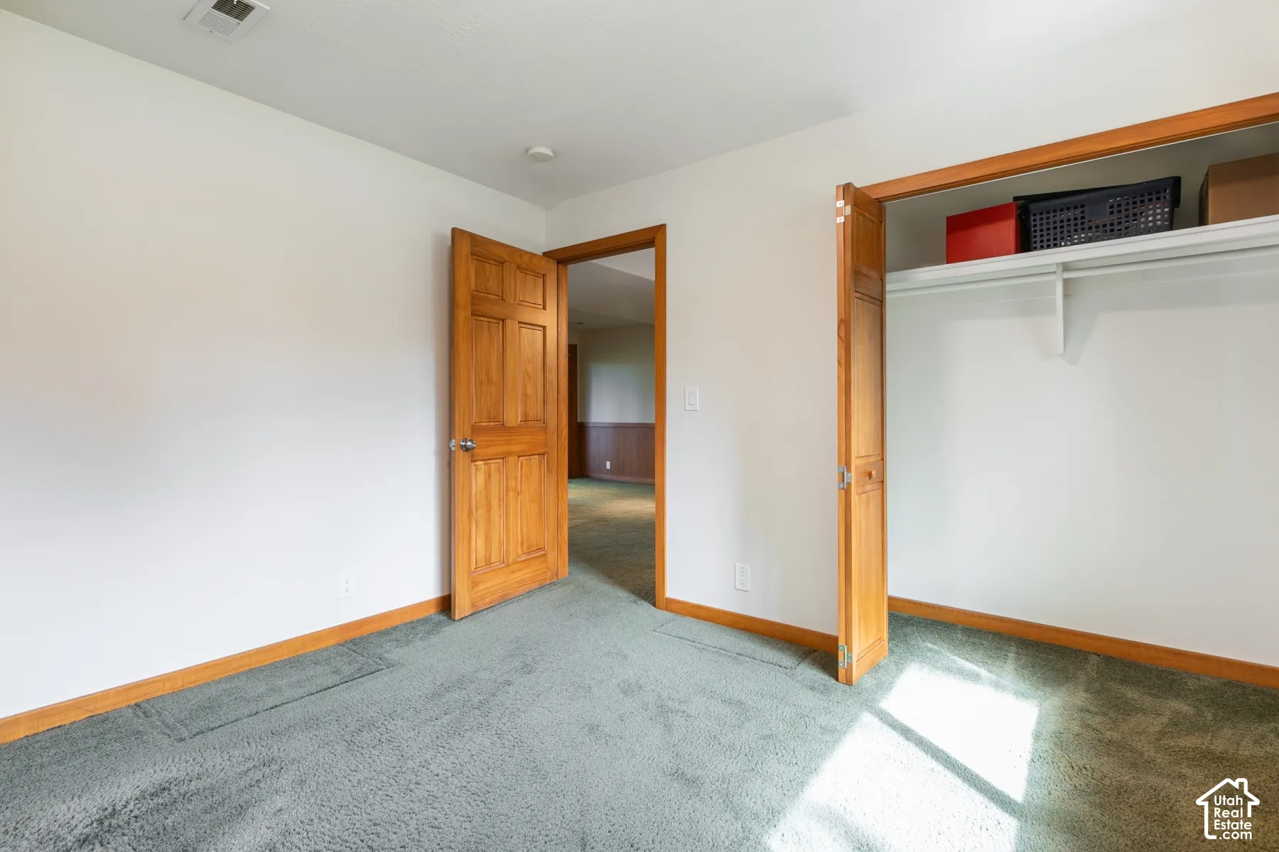 Green carpeting with white walls, wood-finish door, and built-in closet with shelving and hanging rod