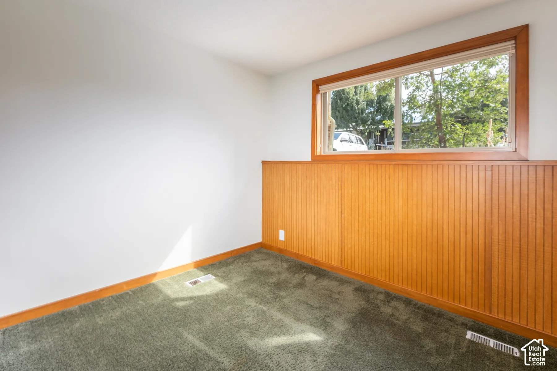 Carpeted flooring, wood-paneled walls, and a large window with wood trim