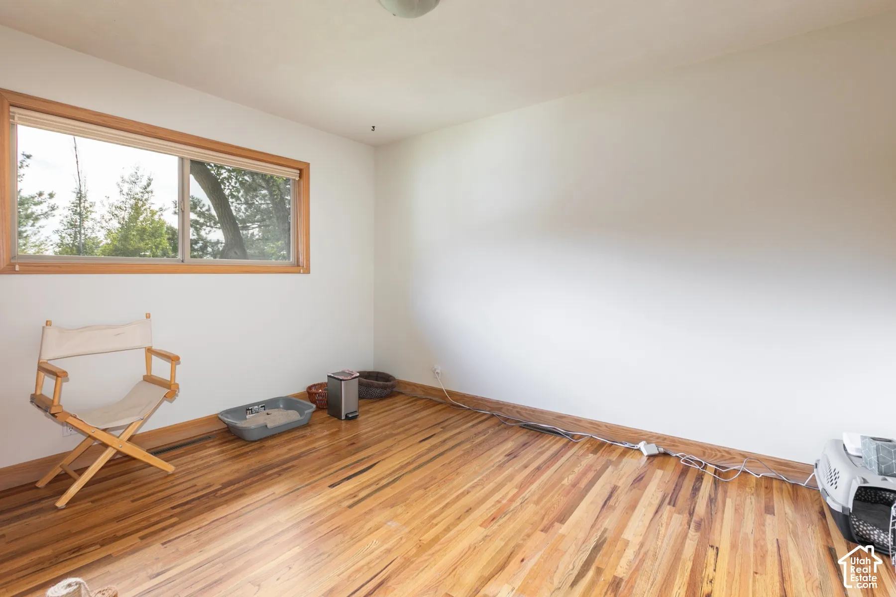 Wood-finish flooring with perimeter baseboards, a window with wood trim, and painted white walls