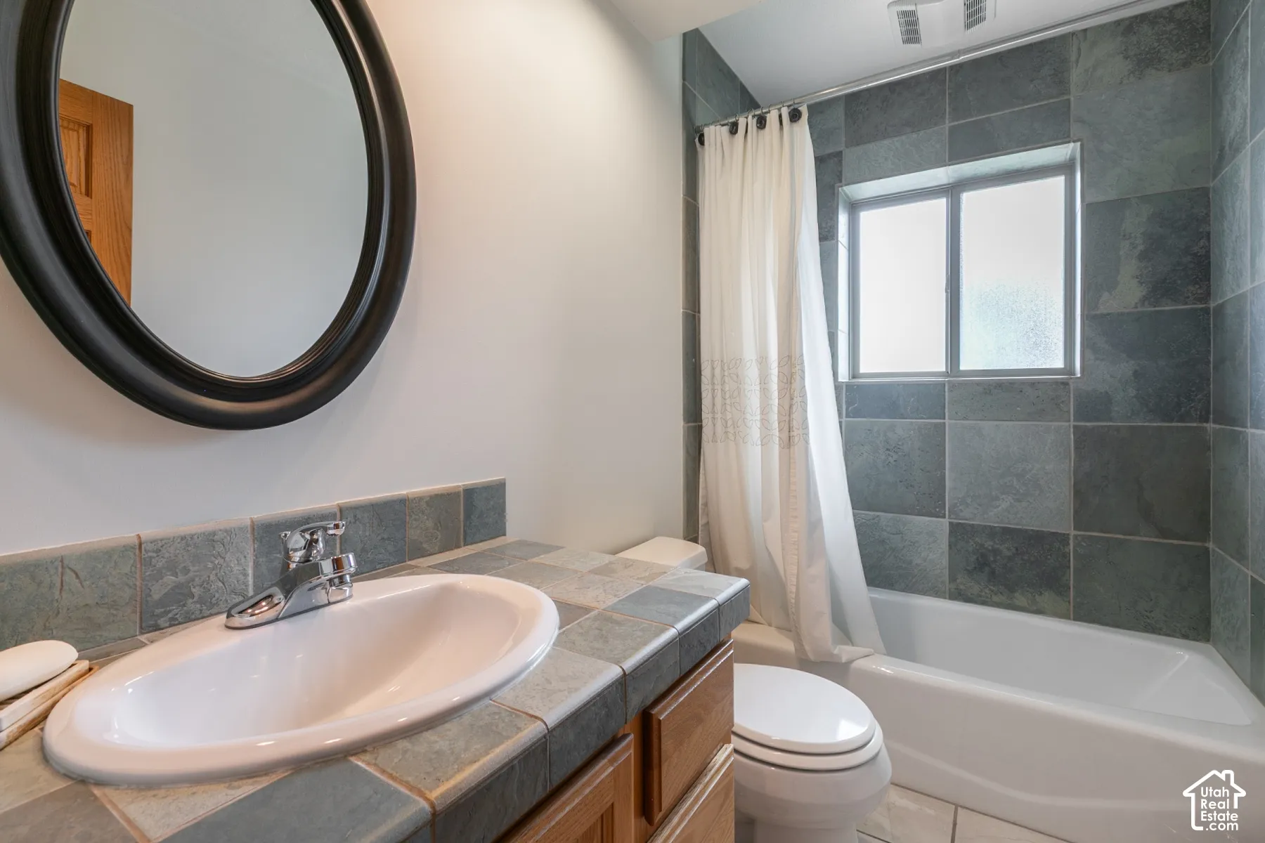 Bathroom featuring a vanity with wood-finish cabinetry, tile countertop, and an oval sink