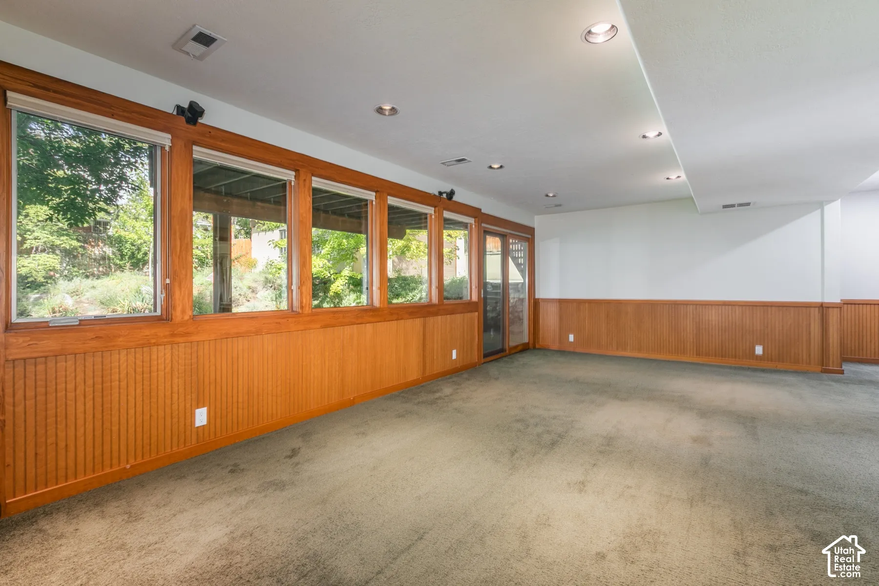 Recessed lighting, wood-paneled wall trim, a series of windows, and a glass-paneled door