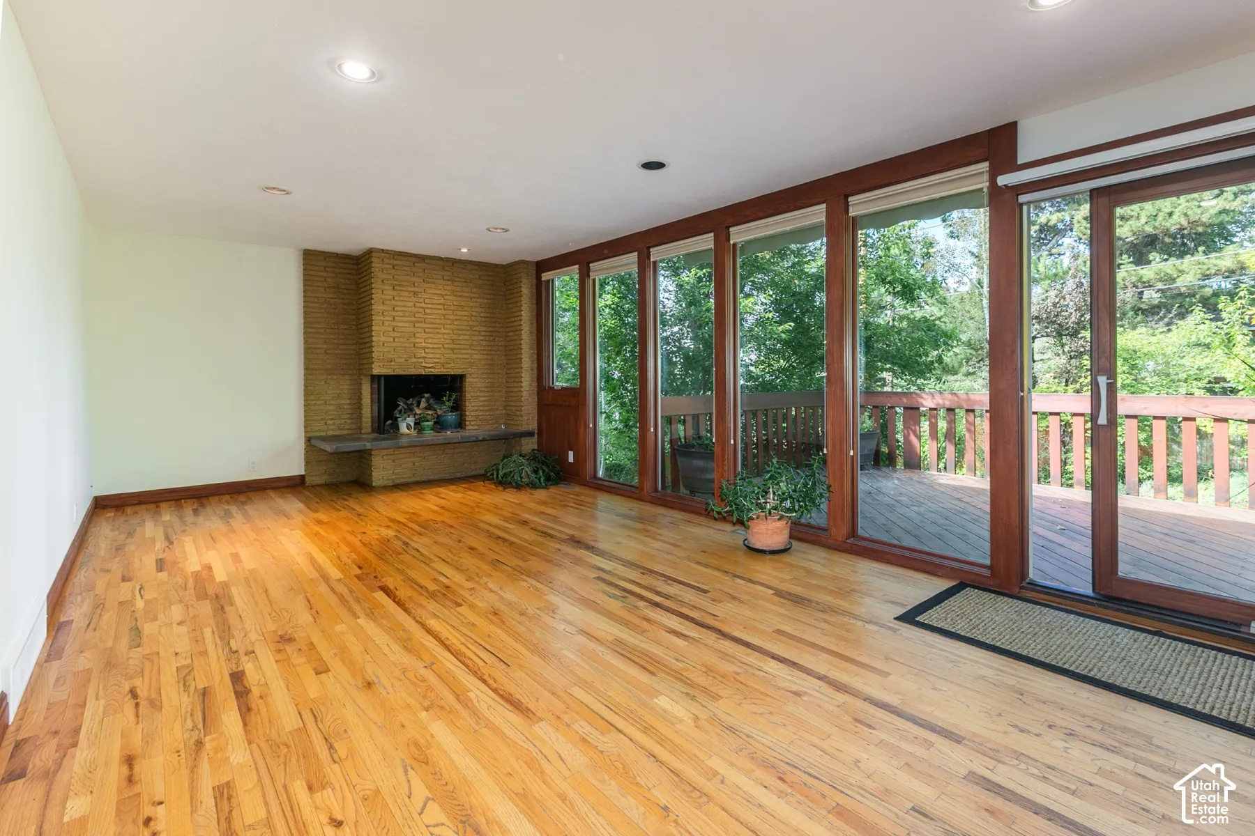 Hardwood flooring, brick-clad fireplace with hearth, recessed lighting, expansive glass doors, and a private deck
