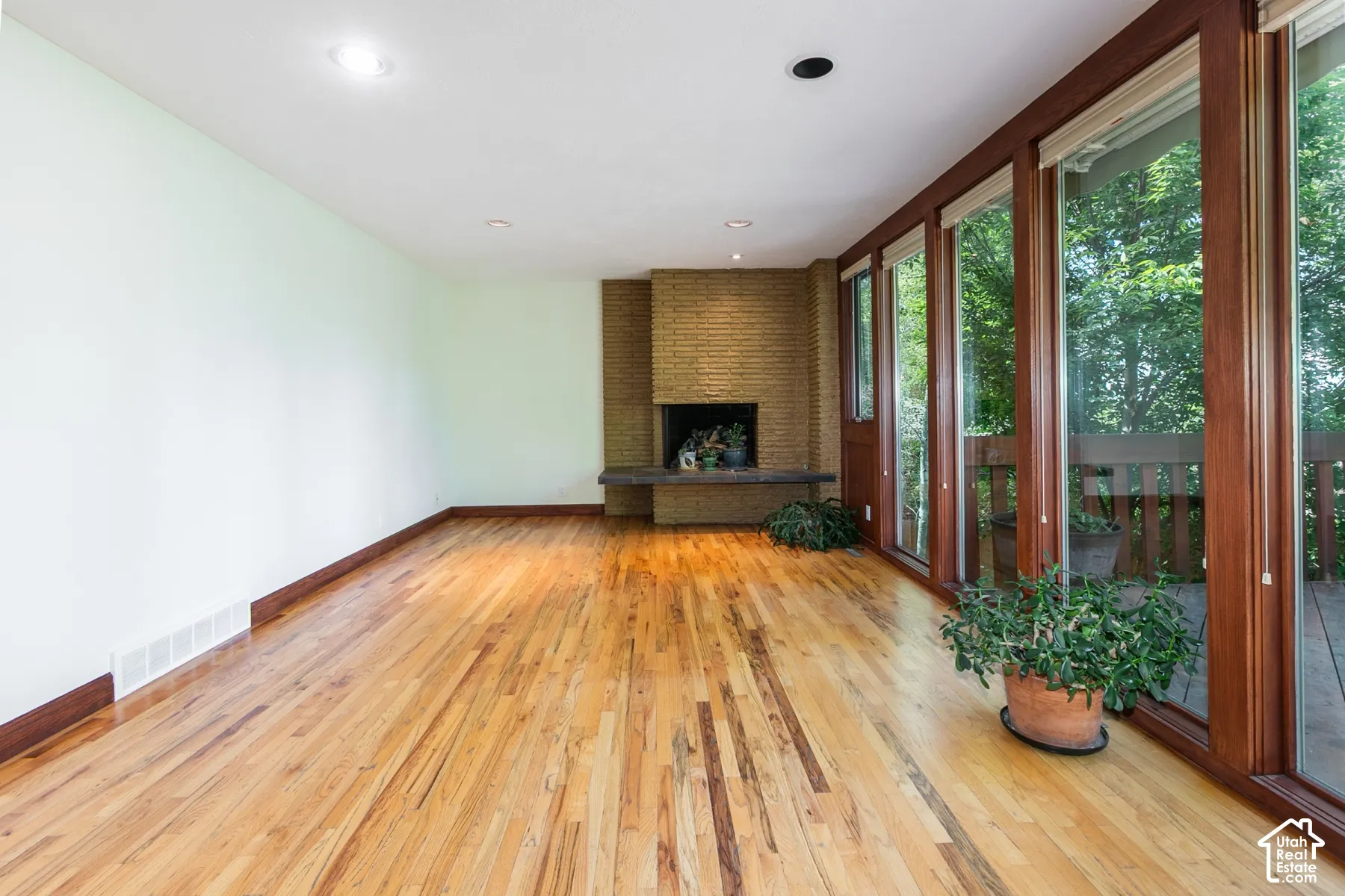 Hardwood flooring, brick fireplace with stone hearth, recessed lighting, and expansive windows