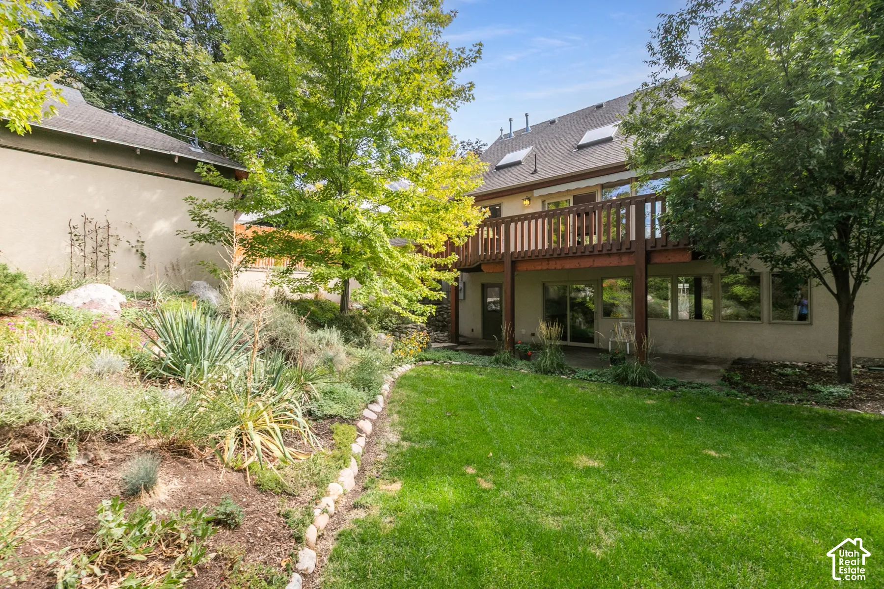 Manicured lawn with mature trees, multi-level deck, lower patio, and skylights