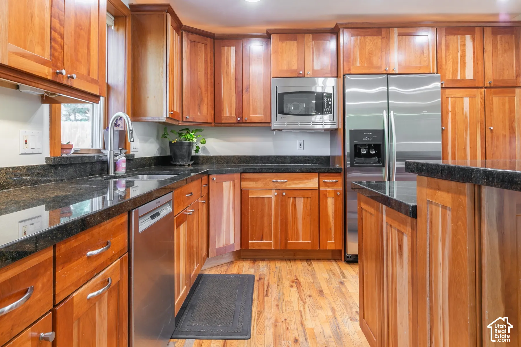 Wood-finish cabinetry with dark countertops, a stainless steel refrigerator, and wood-finish flooring