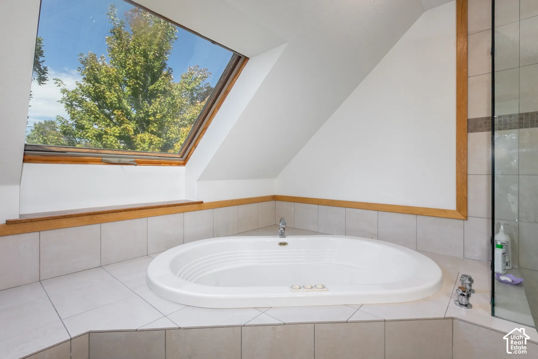 Soaking tub with integrated faucet, tiled surround, and sloped ceiling with an architectural skylight